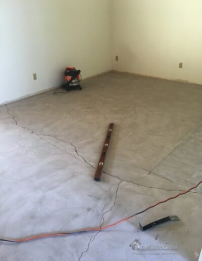 Image shows a cleaned concrete subfloor, a four foot level and large cracks in the slab.